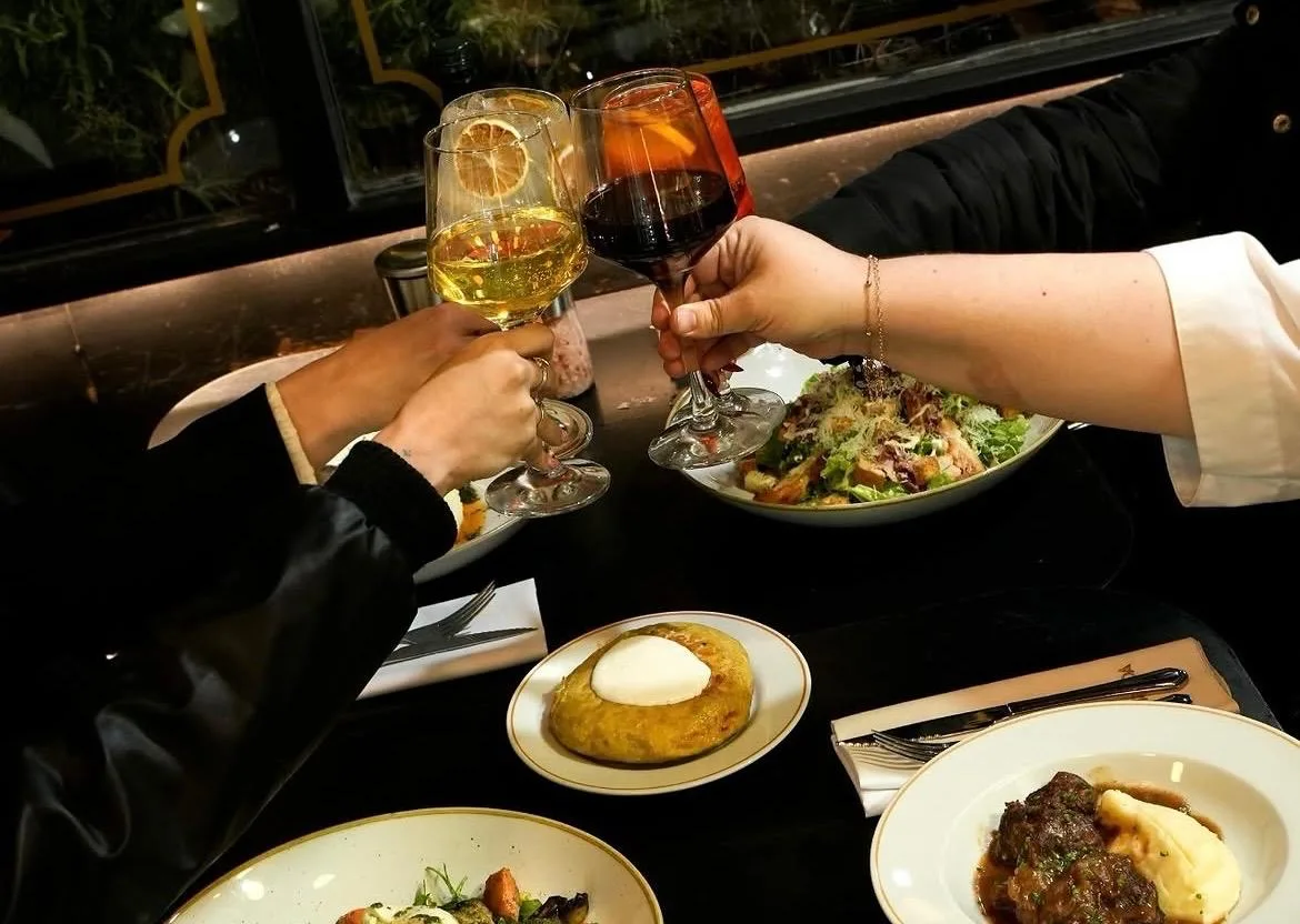 Brindis con copas de vino blanco y un trago de naranja sobre la mesa en Merienda