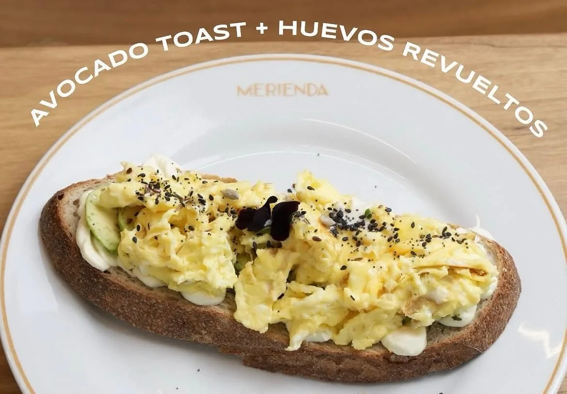 Tostada de pan de masa madre con palta y huevos revueltos en un plato de Merienda